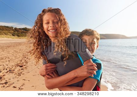 Portrait Of Two Children Wearing Wetsuits Standing By Waves On Summer Beach Vacation