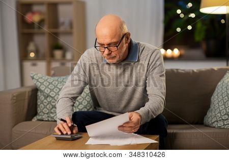 savings, annuity insurance and people concept - senior man with papers or bills counting on calculator at home in evening