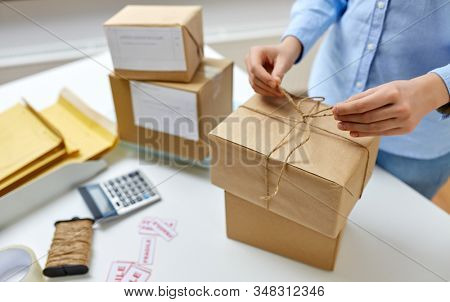 delivery, mail service, people and shipment concept - close up of woman packing parcel box and tying rope at post office