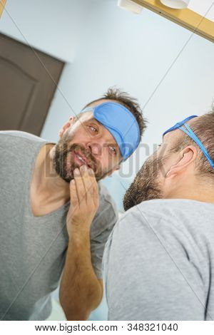 Adult Man With Eyemask On His Forehead Feeling Fresh After Waking Up, Looking At Himself In Bathroom