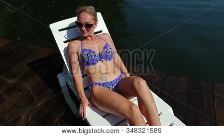 Woman Lie On A Sunbed In Sunglasses And Swimming Suit. Girl Rest On A Flood Wood Underwater Pier. Cl