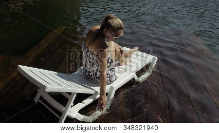 Woman Lie On A Sunbed In Sunglasses And A Boho Silk Shawl. Girl Rest On A Flood Wood Underwater Pier