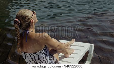 Woman Lie On A Sunbed In Sunglasses And A Boho Silk Shawl. Girl Rest On A Flood Wood Underwater Pier