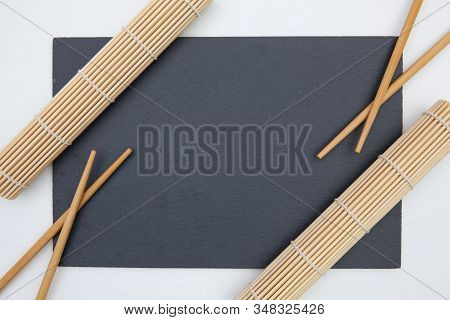 Rectangular Slate Plate With Chopsticks, Bamboo Mat  For Sushi On The White Table. Food Design