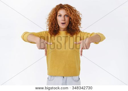 Excited, Curious Redhead Female With Curly Hair, Wear Yellow Sweater, Pointing Down And Looking Amaz