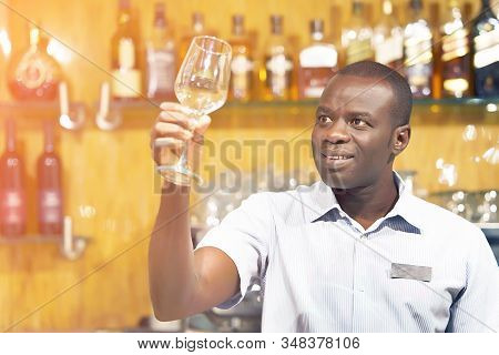 Portrait Of African Elderly Bartender Cleans The Glass. A Handsome African Bartender Polishes A Glas