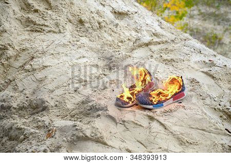 Burning Sports Sneakers Or Gym Shoes On Fire Stand On Sandy Beach Coast. Athlete Burned Out. Physica