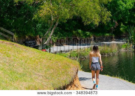 Teenage Girl Walking Away Along A Path Around Lake At Mclaren Falls Park, Tauranga New Zealand
