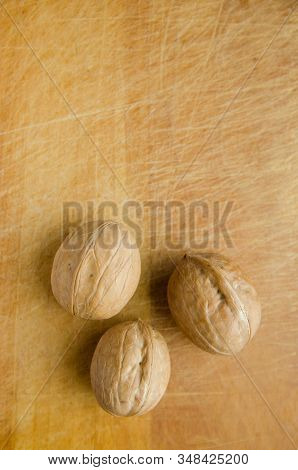 Three Walnuts On Vintage Wooden Cutboard With Knife Marks. Vertical View.