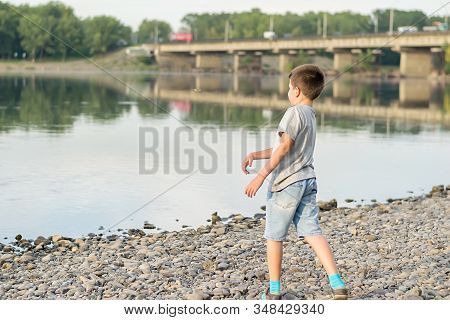 A Child, A Teenager, On A Stony Shore Throws Stones Into The River