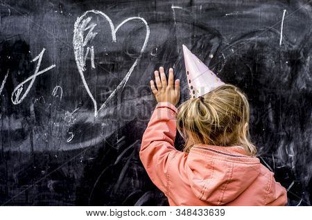 Girl In A Holiday Cap Draws A Heart With Chalk. Valentine Day Concept.