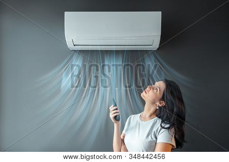 A Beautiful Girl Stands Under Air Conditioning And A Stream Of Fresh Cold Air Against A Gray Wall. T
