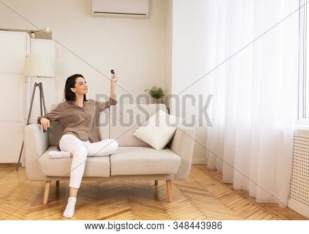 Split System. Satisfied European Girl Holding Remote Control Relaxing Under The Air Conditioner, Sit