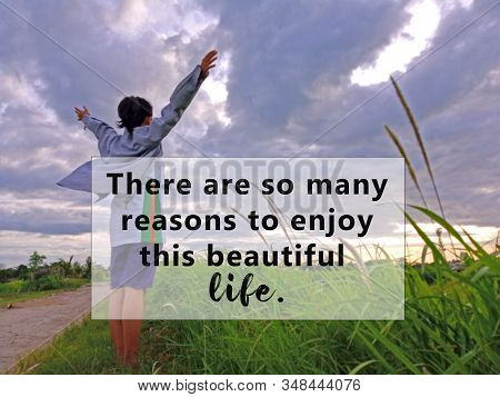 Inspirational quote - There are so many reasons to enjoy this beautiful life. With blurry background of young woman standing alone, raised hands against blue sky over the field view. Life motivational words concept.