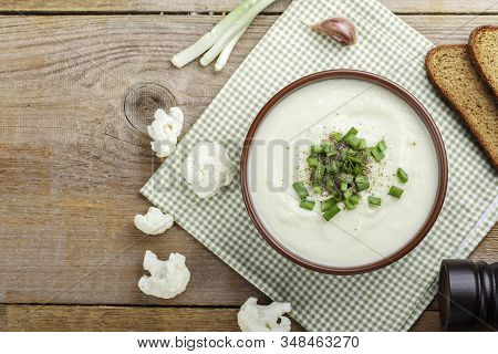 White Vegetable Cream Soup Of Cauliflower In A Brown Clay Plate On A Wooden Background. Simple Diet 