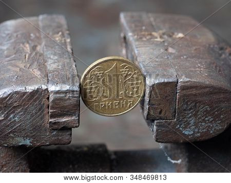 Hryvnya Coin Clamped In A Metal Vise. Currency And Ukrainian Economy Under The Onslaught, The Concep