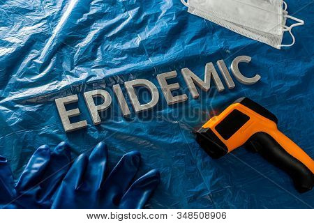 The Word Epidemic Laid By Metal Letters On Crumpled Blue Pastic With Face Masks, Blue Rubber Glove A