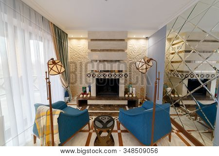 Living room interior with fireplace. Beautiful interior with a large mirror and two blue armchairs. Reflection in the mirror. Floor lamp.