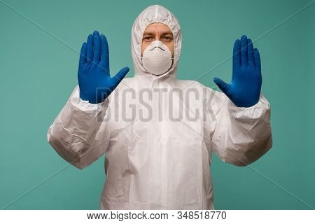 A Male Doctor In Protective Overalls And A Mask Shows Stop Sign. Coronovirus Protection Concept In C