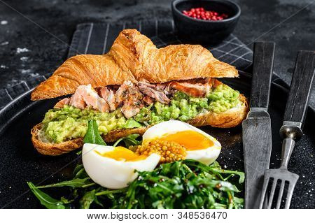 Croissant With Hot Smoked Salmon, Avacado, Arugula And Egg. Black Background. Top View