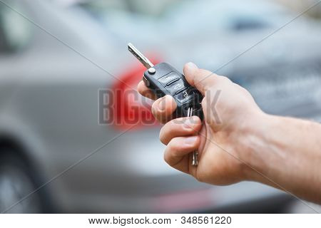 Close Up Hand Of Man Holding Car Key  With Blurred Car On Background. Hand Presses On The Remote Con