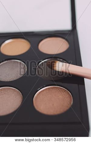 Close-up Of Brush On Top Of Eyeshadow Palette With Trendy Nudes And Bronzy Tones