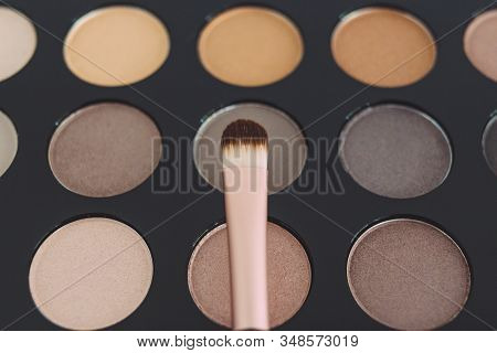 Close-up Of Brush On Top Of Eyeshadow Palette With Trendy Nudes And Bronzy Tones
