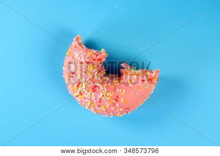 Pink Frosted Donut With Colorful Sprinkles With Bite Missing. On Blue Background .