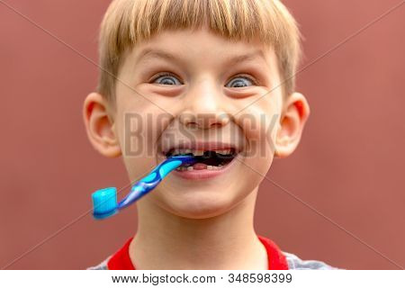 The Boy Holds The Toothbrush In His Teeth With The Reverse Side