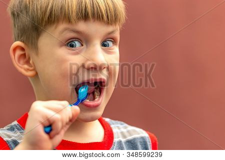 The Child Holds A Toothbrush In His Hand Near His Mouth