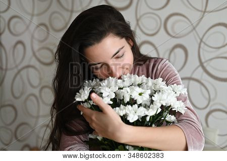 Girl Sniffs A Bouquet Of White Flowers. Brunette Hugs Sniffs A Bouquet Of Delicate Flowers From Her 