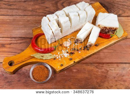 Pieces Of Partly Cut Salted Pork Fatback On Skin Lie On Wooden Cutting Board Among The Some Spice On