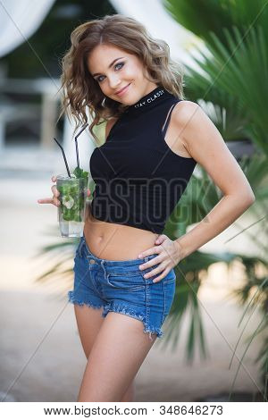 Beautiful Young Woman Enjoy Enjoys A Smoothie And Relax On Tropical Beach With Palm Tree. Summer Vac