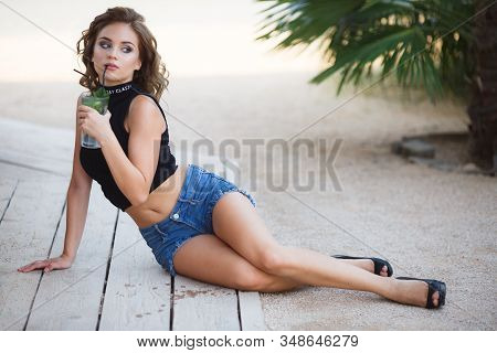 Beautiful Young Woman Enjoy Enjoys A Smoothie And Relax On Tropical Beach With Palm Tree. Summer Vac