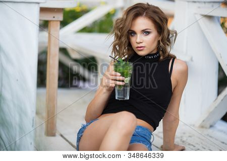 Beautiful Young Woman Enjoy Enjoys A Smoothie And Relax On Tropical Beach With Palm Tree. Summer Vac