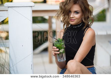 Beautiful Young Woman Enjoy Enjoys A Smoothie And Relax On Tropical Beach With Palm Tree. Summer Vac
