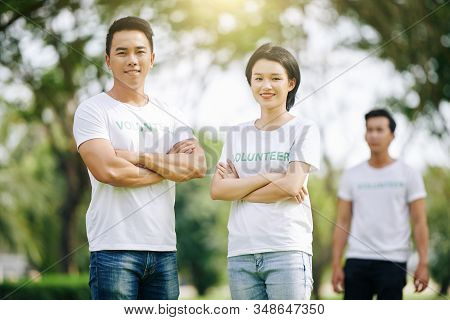 Young Asian Volunteering Stundents Standing In Park With Arms Folded And Smiling At Camera