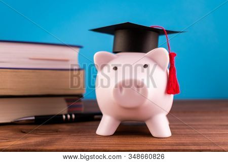 Piggy Bank With A Graduation Hat And A Lot Of Books And A Pen On A Light Blue Backround. Student Sco