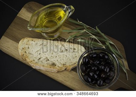 Olives With Olive Oil And Bread On Wooden Board. On Black Background.