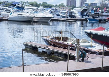 Motor Boat Anchored On A Rope At The Pier Against The Background Of Blurry Yachts