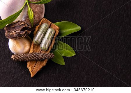 Herbal Medicines Concept. Ayurvedic Capsules With Green Herbs, Whole Spices On Black Background And 