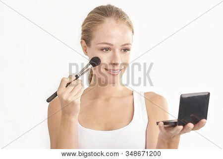 Close-up Studio Shot Of Beautiful Young Woman Holding Hand Makeup Palette And Brush While Applying M