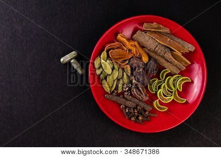 Top View Of Cinnamon, Dry Ginger, Mace(javitri) And Two Herbal Tablets With Green Leaves On A Black 