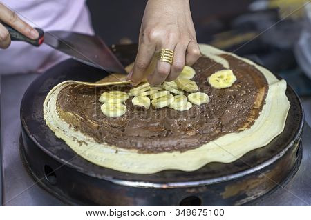 Thai Pancakes Preparation: The Cook Wraps A Pancake With A Spatula With Chocolate Paste And A Banana