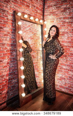 Fat Plump Charming Cute Woman With Black Curly Hair In Black Beautiful Dress In The Room With Mirrow