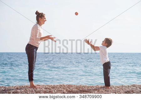 Active Mother Female And Happy Small Kid Playing Leisure Games On Sea Beach Throwing Apple In Air