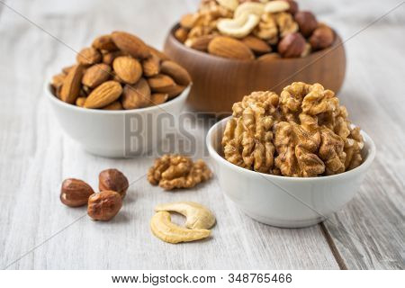 Different Nuts In White And Wooden Bowls On Wood Table