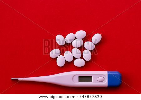Electronic Thermometer And Pills On A Red Background. Means For Treating Flu And Colds, Lowering The