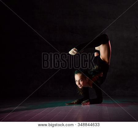 Young Girl Gymnast In Black Sport Body And Uppers Lying On Floor On Neck With Streched Back And Body