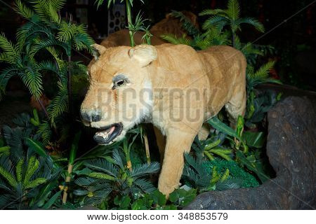 Statue Lion . Life Size Replica Model . The Lion Is In An Artificial Green Forest At Night . Brown L